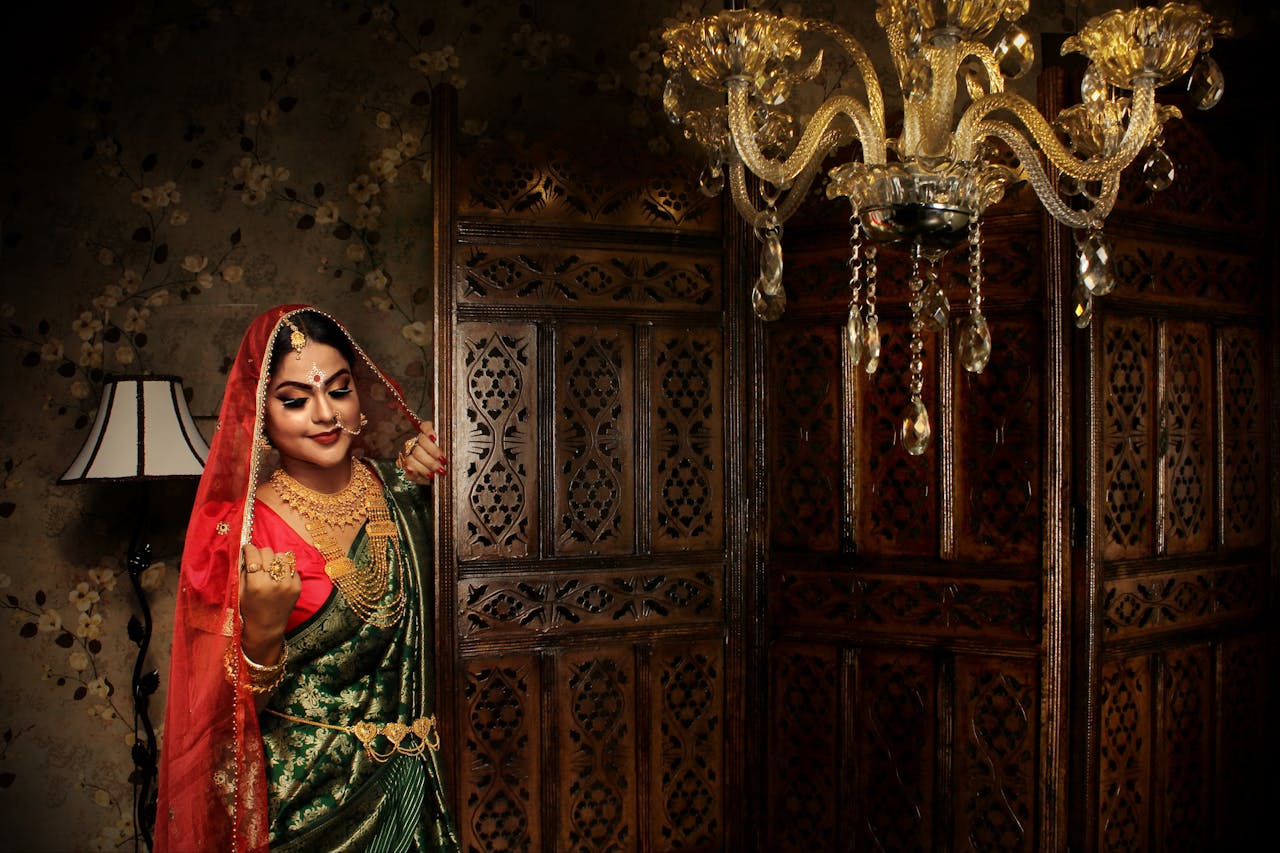 Beautiful Indian bride in a traditional sari with ornate jewelry, posing indoors under a chandelier.